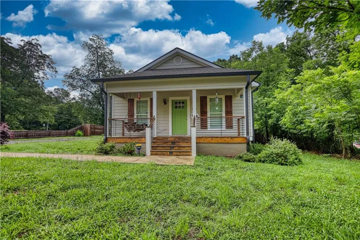 Single-story home featuring a covered front porch with wood flooring, white columns, and a bright green front door