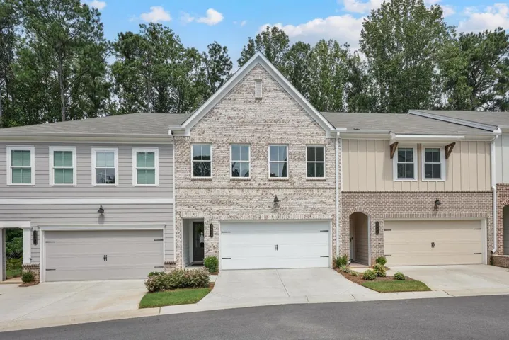 Contemporary townhome with a light brick facade, white trim windows, two-car garage, and a peaked roofline