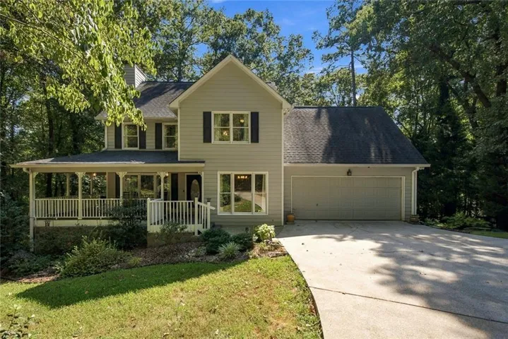 Two-story residence featuring light siding, a covered front porch with white railings, a two-car garage, and a concrete driveway