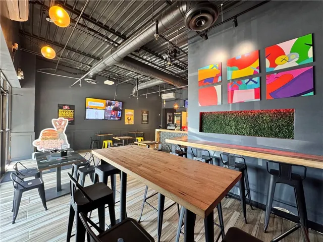Exposed industrial-style ceiling with ductwork, multiple flat-screen displays, decorative wall panels, a built-in planter box, and a high-top wood-finish counter