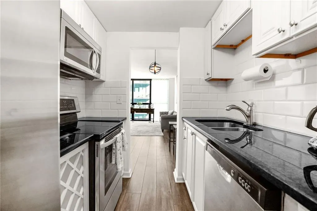 Kitchen with stainless steel appliances, white cabinets, dark stone counters, dark wood-style flooring, and hanging light fixtures