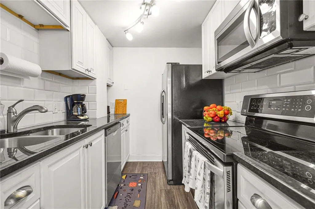 Kitchen featuring stainless steel appliances, decorative backsplash, and white cabinets