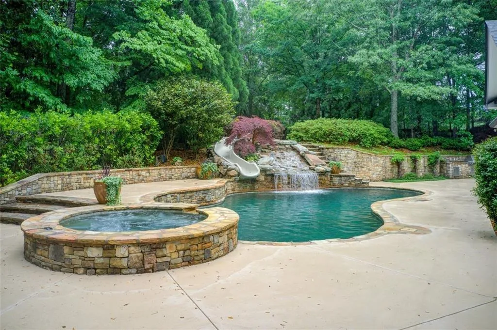 Spa, slide and waterfall with lush  landscaping.