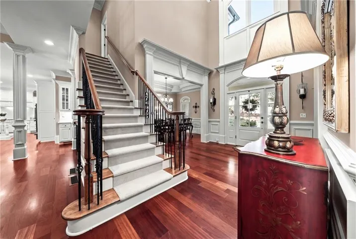 Two-story foyer with rich wood-finish flooring, a grand staircase with wrought iron balusters, and extensive crown molding