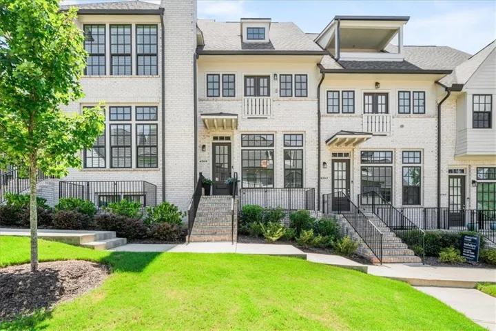 White brick townhouse exterior featuring black grid windows, black railings, and a covered entry