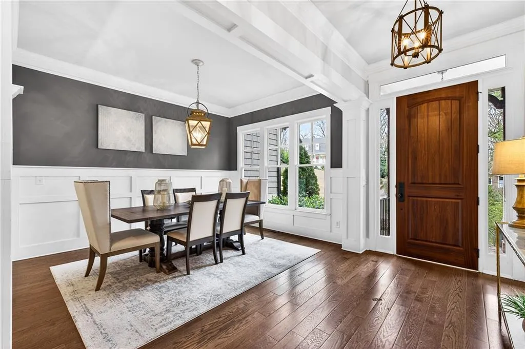 Dining space with crown molding, dark wood flooring,  wainscoting, and chandeliers adorn foyer and dining room