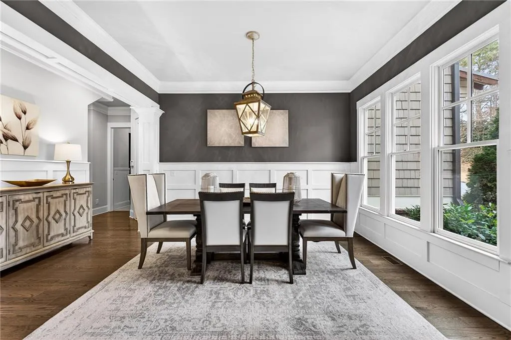 Dining space featuring a wainscoted wall, a decorative wall, dark wood flooring, decorative columns, and ornamental molding