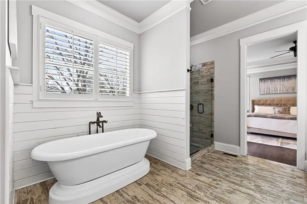 Bathroom with ensuite bath, a shower stall, ornamental molding, wood finished floors, and a freestanding tub