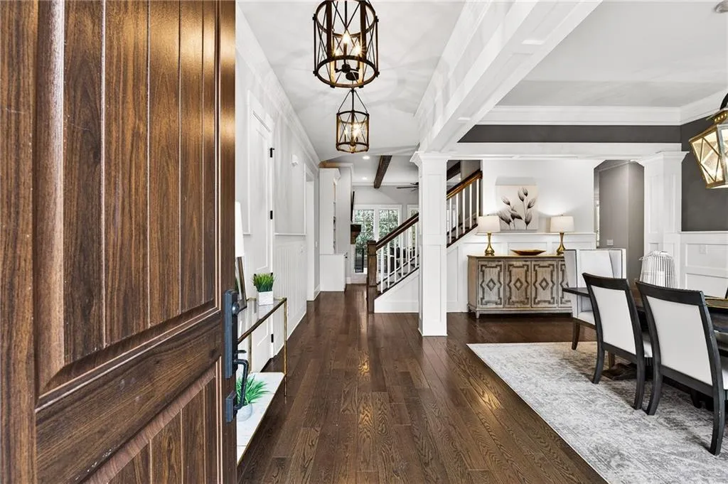 Entryway with columns denoting dining room, dark wood flooring, wainscoting, and stairway to upper level beyond
