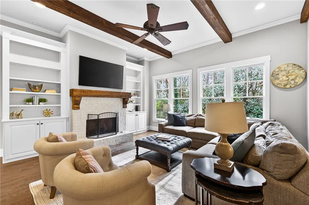 Living room featuring a brick fireplace, a ceiling fan with natural wood mantel and wood beamed ceiling, built in features flank fireplace