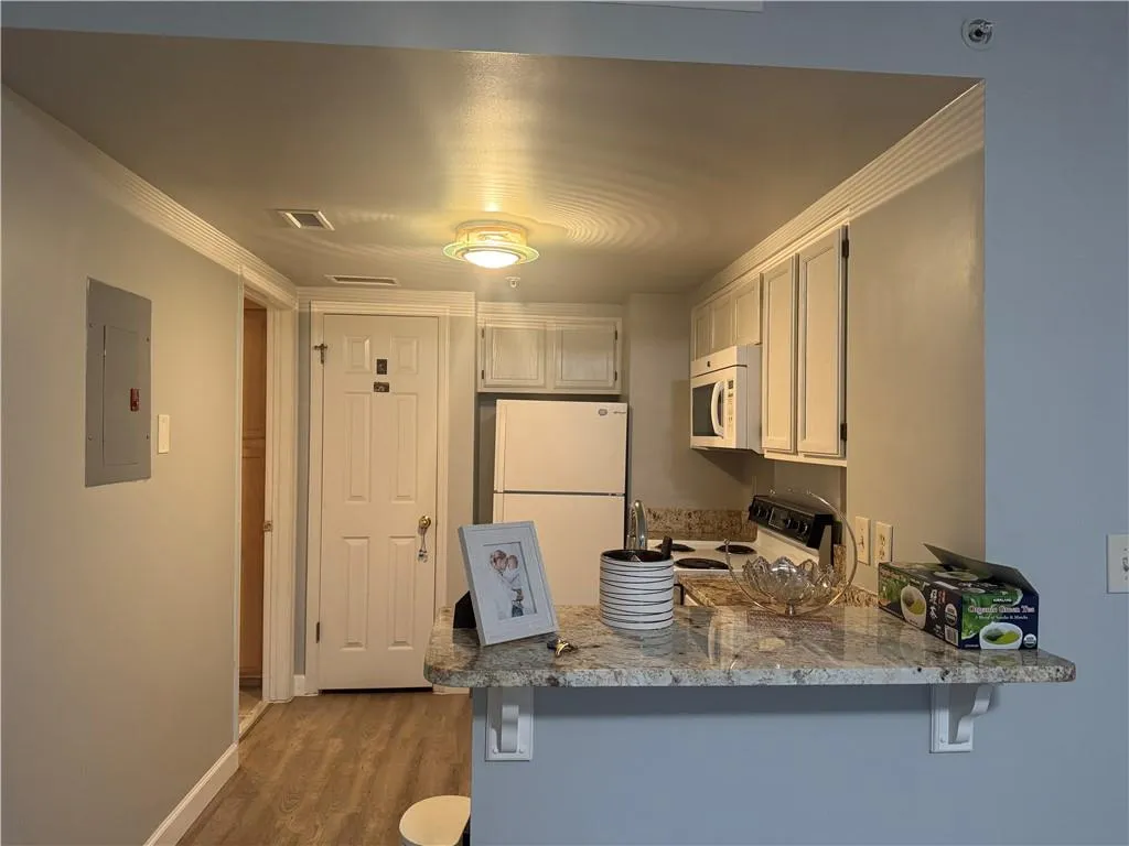 Kitchen with white appliances, a breakfast bar area, dark wood-type flooring, and electric panel