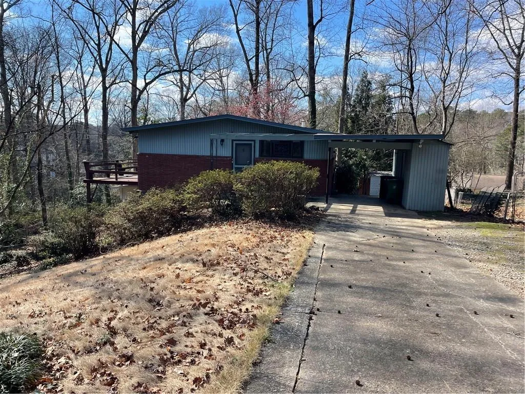 View of front of house with an attached carport, driveway, brick siding, and a wooden deck