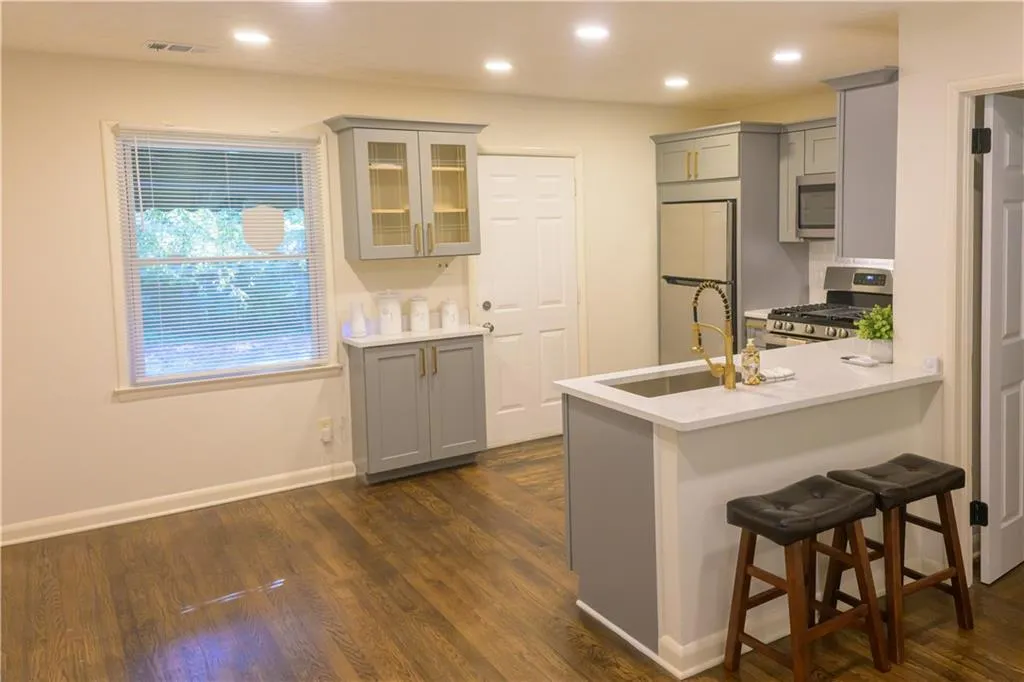 Kitchen featuring gray cabinets, appliances with stainless steel finishes, glass insert cabinets, a breakfast bar, and recessed lighting