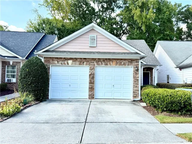 Two-car garage with white paneled doors, stone facade accents, and a shingled roof