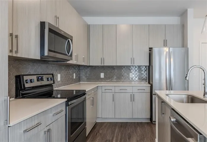 Kitchen featuring light wood-finish cabinetry, stainless steel appliances, a tiled backsplash, light-toned countertops, and wood-finish flooring