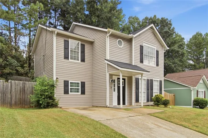Two-story residence featuring light-colored siding, contrasting dark shutters, a covered entry porch, an oval window, and a concrete driveway
