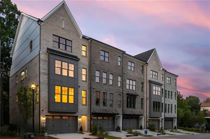 Townhome exterior featuring gray brick, black-framed windows, a prominent gable roofline, and integrated garages