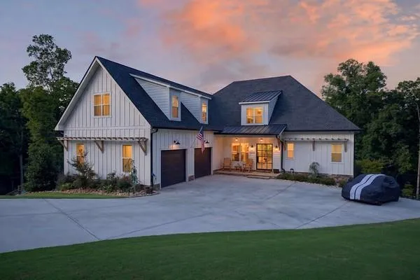 Modern farmhouse exterior featuring white board and batten siding, a dark shingle roof, a two-car garage with dark doors, a concrete driveway, and a covered front porch