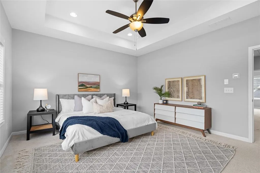 Bedroom with light carpet, multiple windows, recessed lighting, a ceiling fan, and a tray ceiling