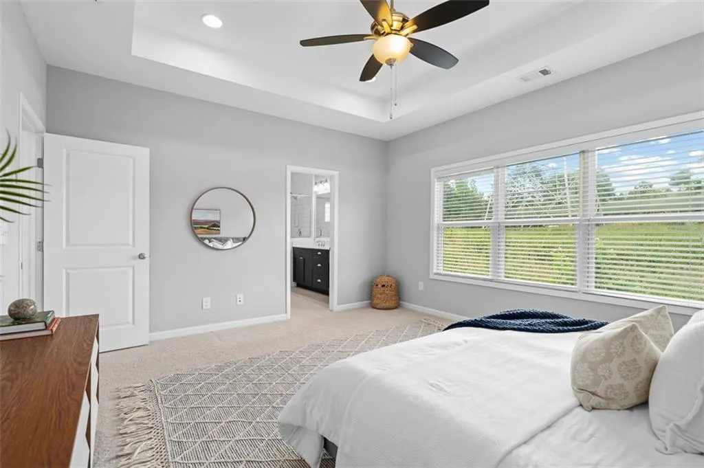 Bedroom featuring a tray ceiling, light colored carpet, ensuite bathroom, and a ceiling fan