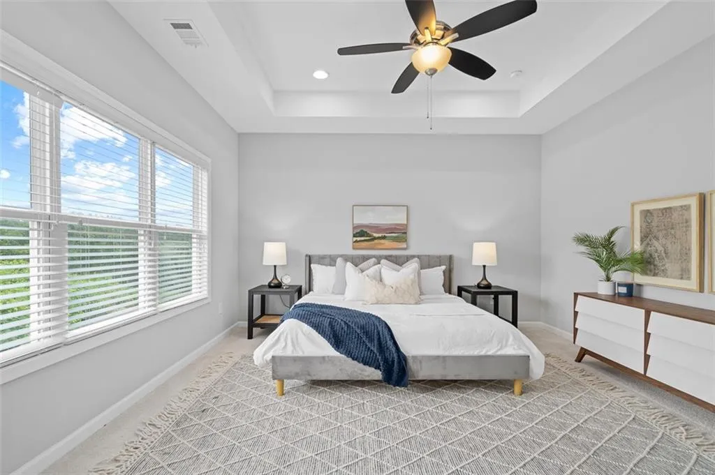 Bedroom with a raised ceiling, light colored carpet, and a ceiling fan