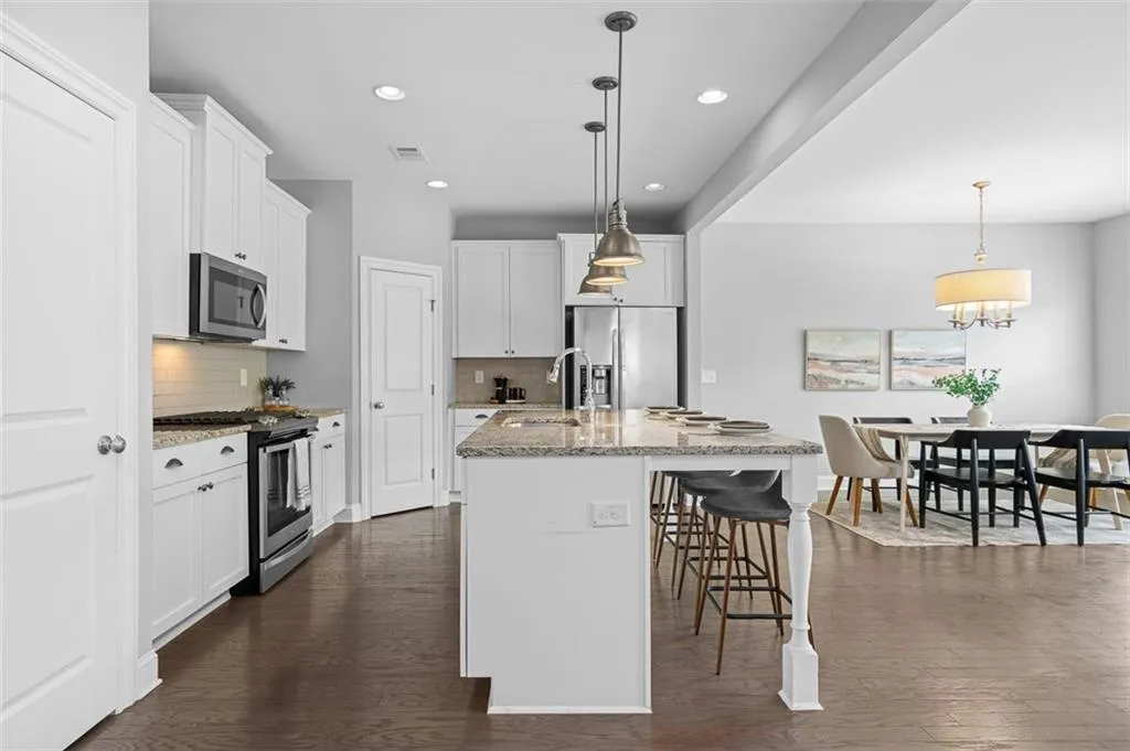 Kitchen with appliances with stainless steel finishes, dark wood finished floors, recessed lighting, tasteful backsplash, and a center island with sink