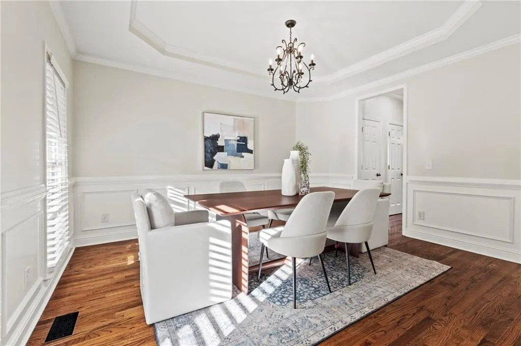 Dining space featuring a chandelier, hardwood floors, decorative molding, a wainscoted walls, and a raised ceiling