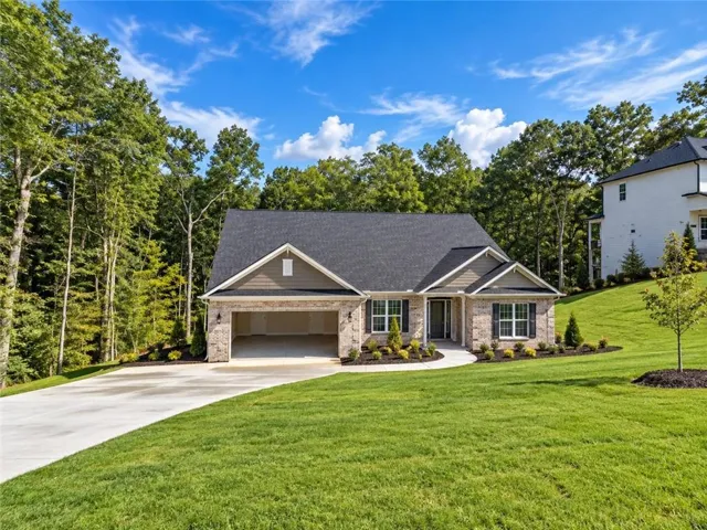Brick and siding exterior with a two-car garage, mature trees, and a concrete driveway