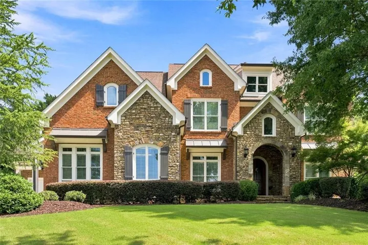 Brick and stone facade featuring multiple gables, arched entry, and dark louvered shutters