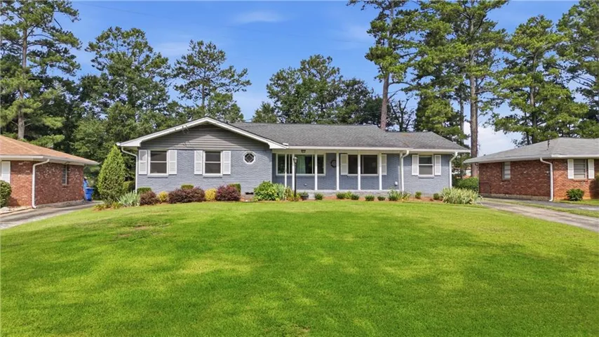 Ranch-style exterior featuring painted brick and siding, a large front lawn, mature perimeter trees, white window shutters, and a covered entry