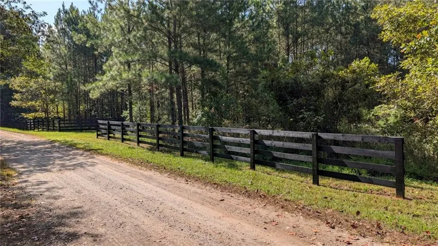Gravel driveway with a dark wood-finish fence and mature trees