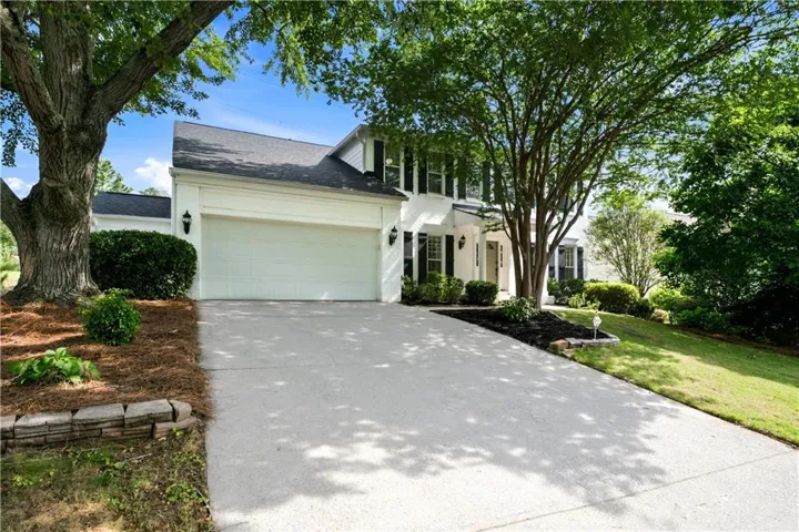 White exterior residence featuring a two-car garage, concrete driveway, and established landscaping