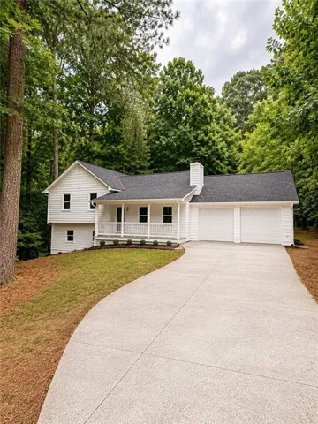 White facade residence featuring a covered front porch, two-car garage, dark shingle roof, and a concrete driveway