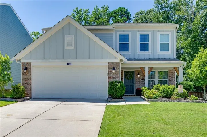 Board and batten siding, brick accents, two-car garage, covered porch with wood beam details, and mature landscaping