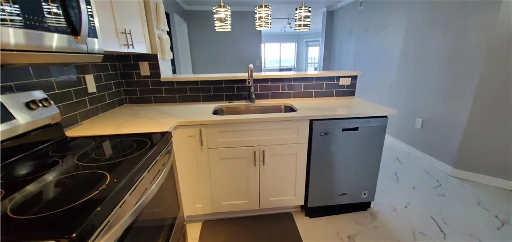Kitchen featuring sink, white cabinetry, crown molding, and stainless steel appliances