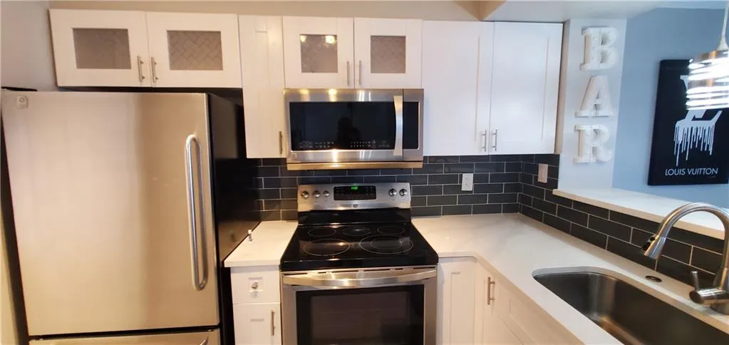 Kitchen featuring sink, appliances with stainless steel finishes, decorative backsplash, and white cabinetry