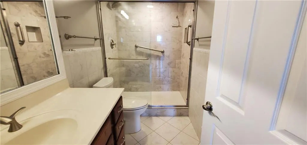 Bathroom featuring vanity, tile patterned floors, a shower with shower door, tile walls, and toilet