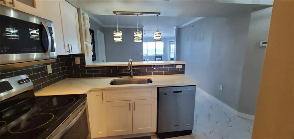 Kitchen featuring tasteful backsplash, ornamental molding, white cabinets, appliances with stainless steel finishes, and sink