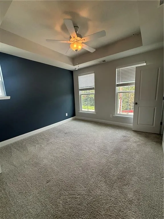 Carpeted empty room featuring a raised ceiling and ceiling fan