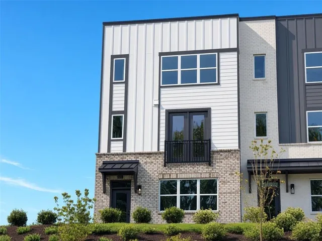 Contemporary exterior with mixed material facade, prominent dark-framed windows, a Juliet balcony, and an awning over the entry