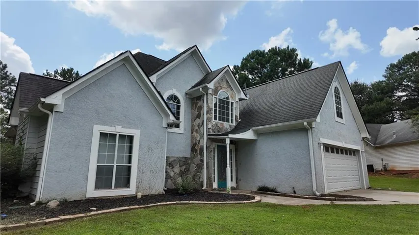 Stucco and stone facade with an arched window accent, an attached garage with a white panel door, and a dark shingle roof