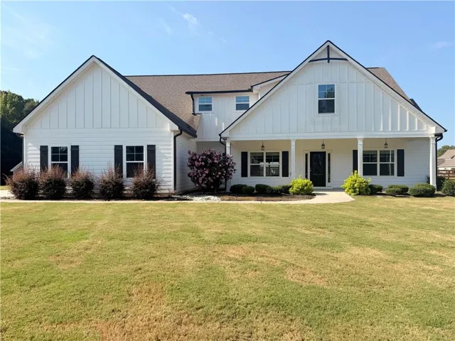 Gabled roofline, board and batten siding, covered front porch with columns, dark roof shingles, and black window shutters