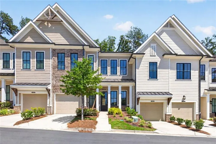 Contemporary townhome facade featuring mixed material siding, black-framed windows, integrated garage, and a covered entry