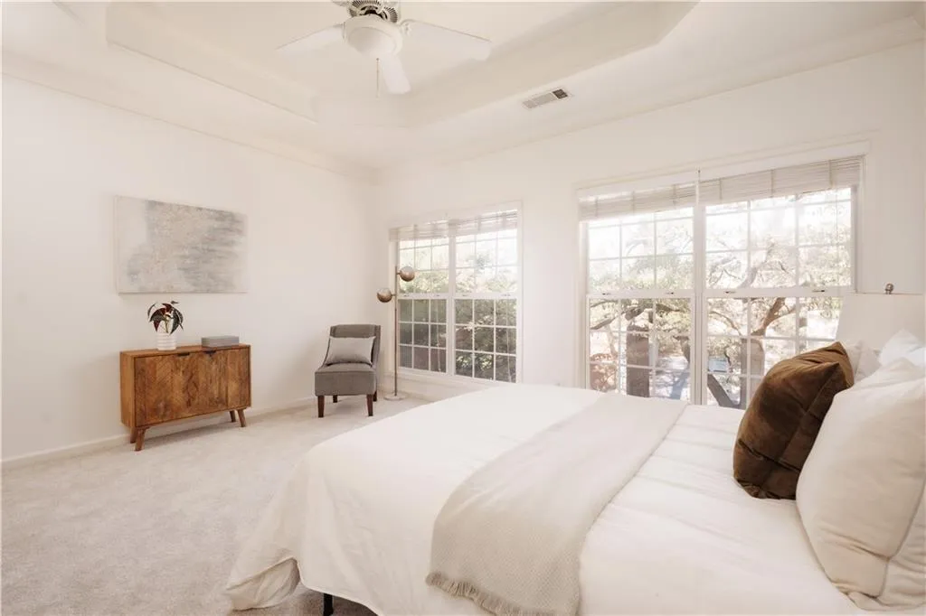 Carpeted bedroom with a raised ceiling, crown molding, and ceiling fan