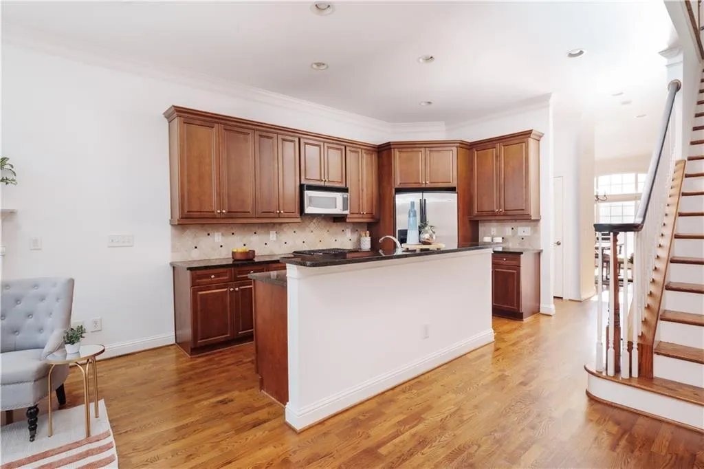 Kitchen featuring tasteful backsplash, a center island with sink, stainless steel refrigerator with ice dispenser, brown cabinets, and ornamental molding