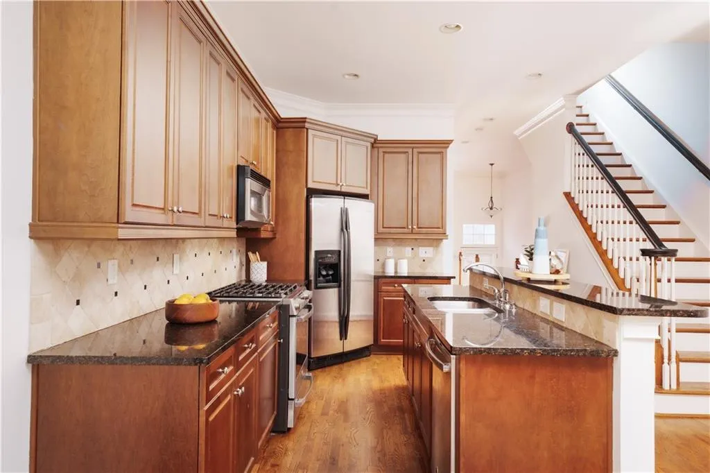 Kitchen with light wood-type flooring, dark stone countertops, stainless steel appliances, a center island with sink, and decorative backsplash