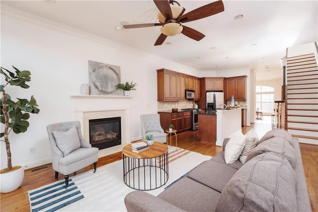 Living room featuring light wood-type flooring, ornamental molding, a glass covered fireplace, a ceiling fan, and stairs