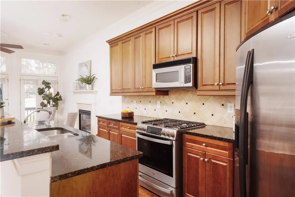 Kitchen featuring stainless steel appliances, ornamental molding, dark stone counters, decorative backsplash, and brown cabinets