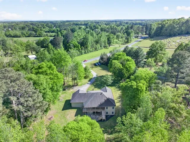 Two-story property with a dark shingle roof and a light-colored exterior, surrounded by extensive mature trees and greenery