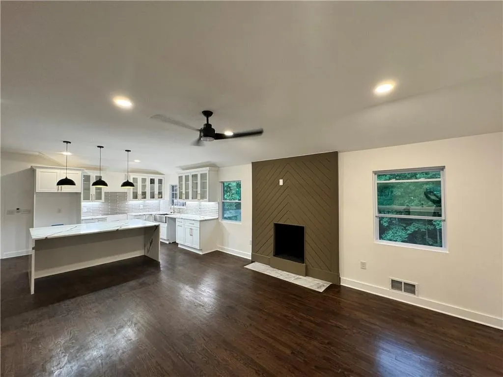 Unfurnished living room with ceiling fan, dark wood-type flooring, and a large fireplace